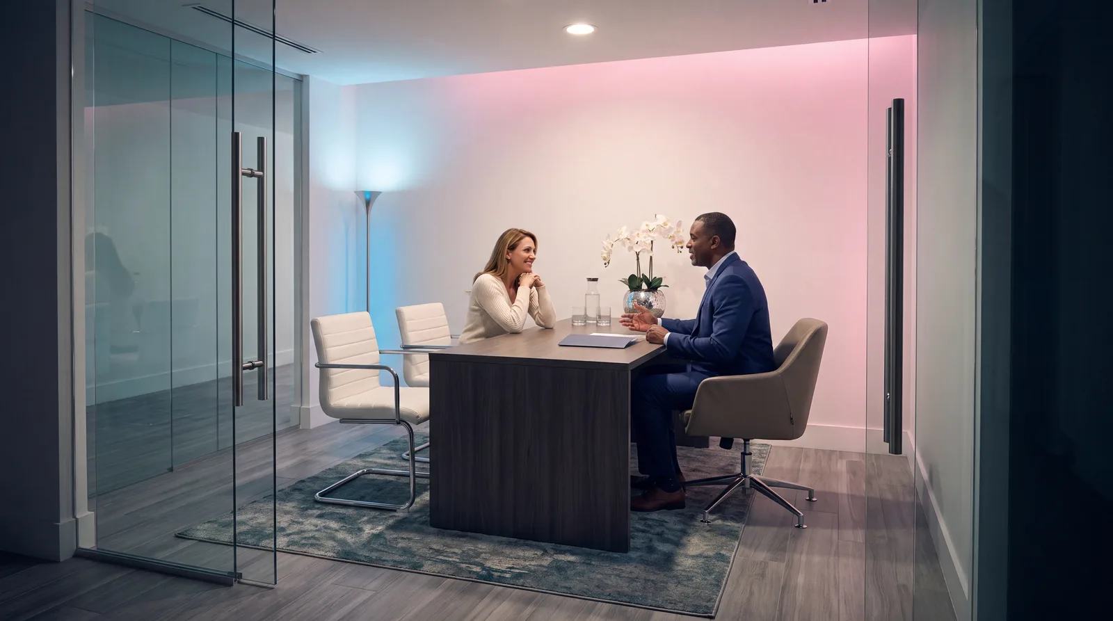 Doctor and woman in her late 40s talk across a desk in a glass-walled Miami clinic consult room