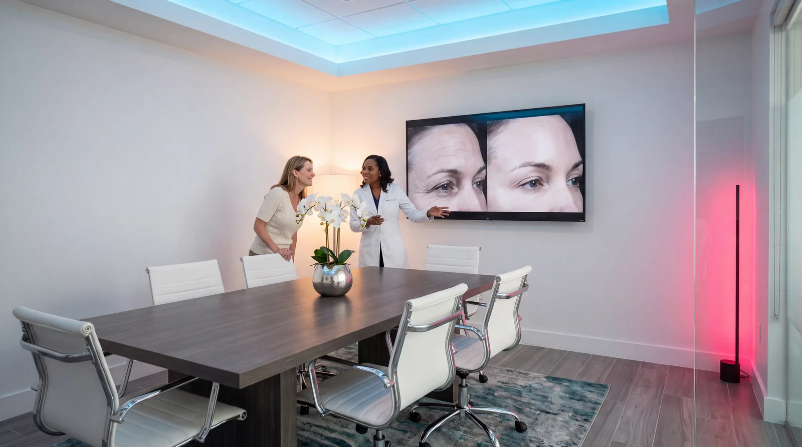 Clinician and patient standing at a wall screen reviewing high-resolution facial photographs of forehead and eye lines