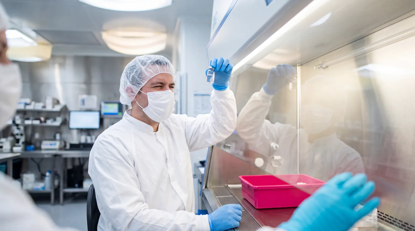 Pharmacy technician inspecting a vial under a sterile compounding hood