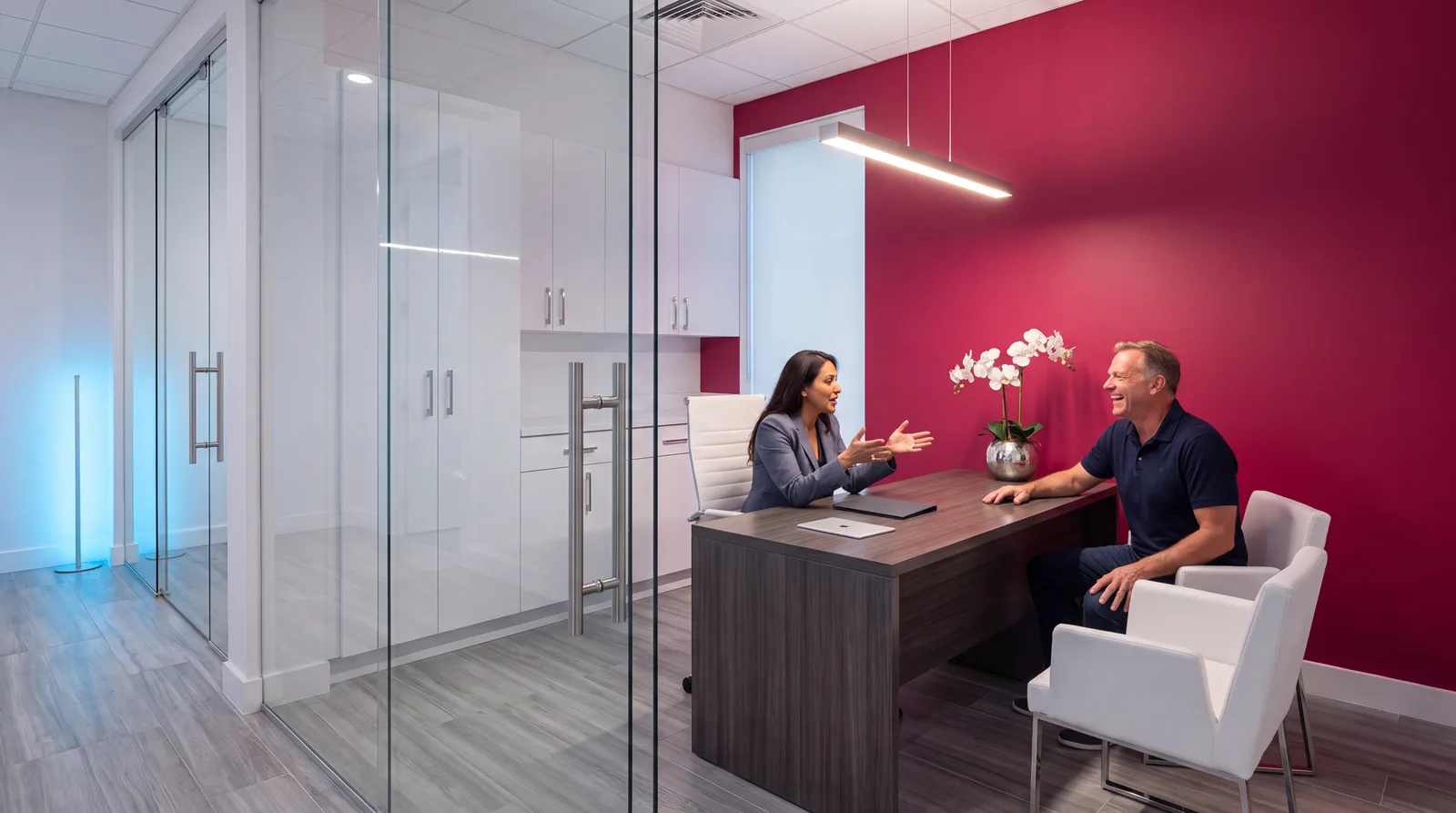 Clinician and male client talking across a desk in a glass-walled Miami consult room, results between them