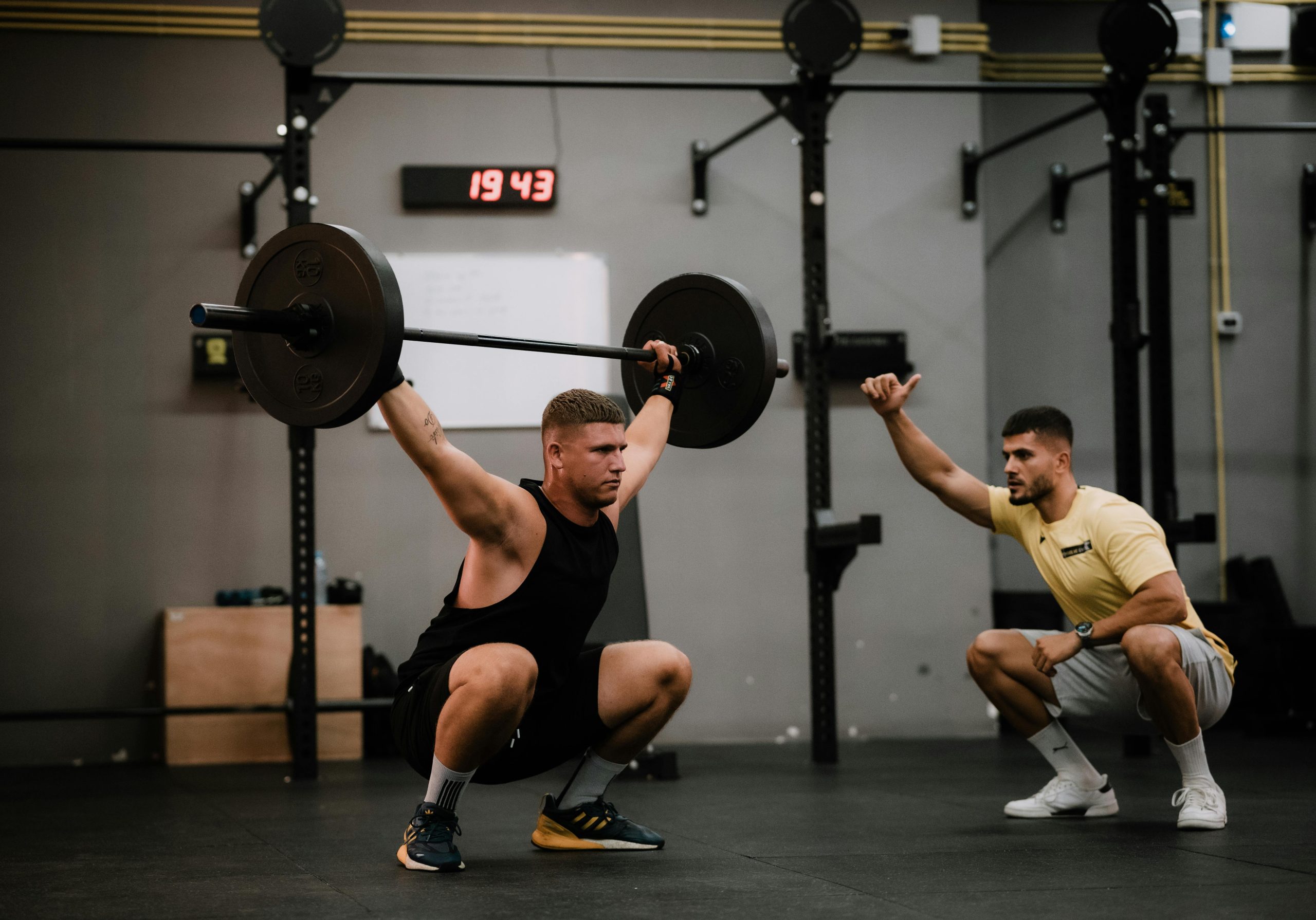 Two men in a gym, with one lifting weights and the other spotting